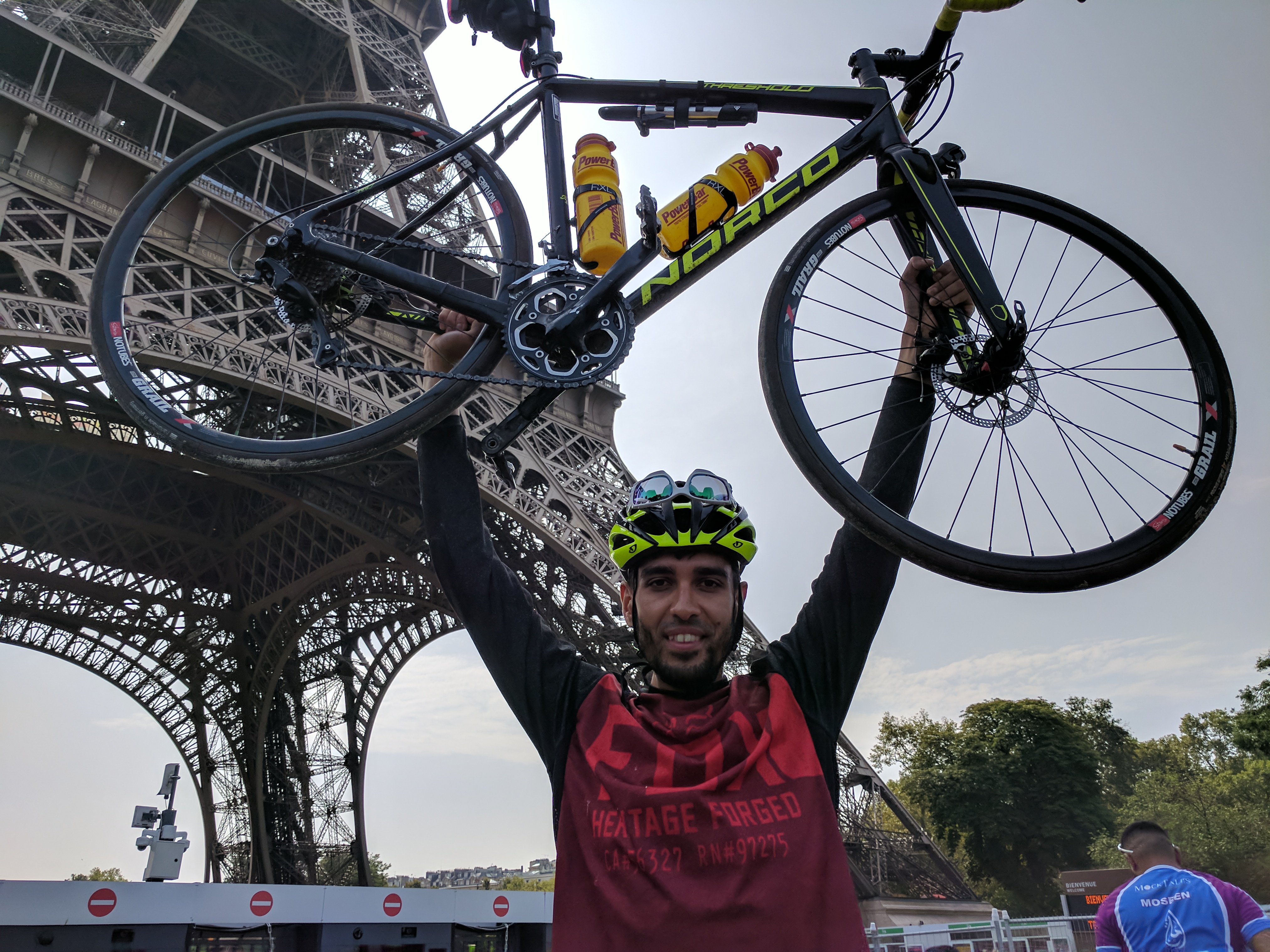 Image:Bari Khan raises his bike aloft in front of the Eiffel Tower in Paris after completing his ride from London in 2017.