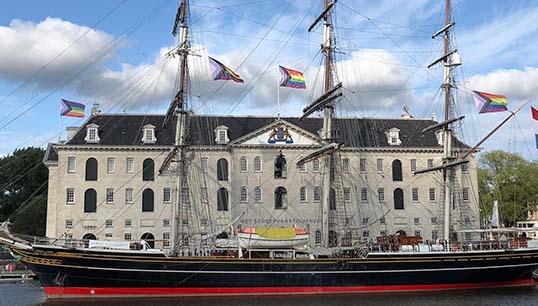 Image:The Netherlands National Maritime Museum with the clipper Stad Amsterdam flying the LGBT+ Pride rainbow flag in August 2021. Image: courtesy of museum